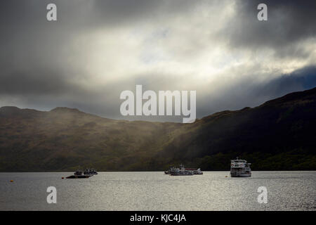 Kreuzfahrtschiffe auf See mit dramatischen Wolken und Licht am Loch Lomond in Schottland, Großbritannien Stockfoto