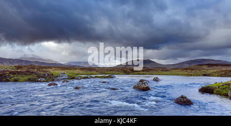 Fluss in Moorlandschaft mit dunklen Sturmwolken und Bergen im Hintergrund bei Rannoch Moor in Schottland, Großbritannien Stockfoto