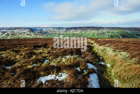 Patches von Schnee über das Heidekraut dominierten Moorland der North York Moors auf einer feinen Winter morgen flankiert von Ackerland, Yorkshire, UK. Stockfoto