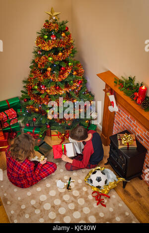 Ansicht von oben der Kinder ihre Geschenke öffnen eingepackten Geschenke zu Weihnachten Morgen neben dem Baum und Kamin. Stockfoto