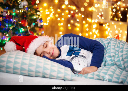 Junge schlafend auf dem Bett mit Uhr in der Nähe von Weihnachten Baum Stockfoto