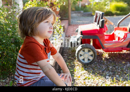 Nachdenklich kaukasischen Jungen in der Nähe von Spielzeug Auto sitzen Stockfoto