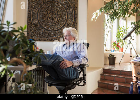 Kaukasische Mann trinkt Kaffee mit Füßen auf Schreibtisch Stockfoto