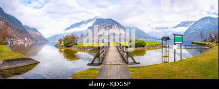 Spätherbst Panorama mit den Hallstätter See, den österreichischen Alpen, die Insel auf dem See und eine hölzerne Brücke auf sie zugreift, in Hallstatt Stadt Stockfoto