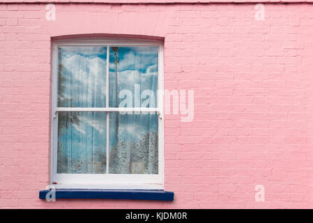 Viktorianisches Fenster mit weißen Holzmöbeln Schärpe, weiße Vorhänge und blauen Balkon auf einem hellen rosa bemalten Wand Stockfoto