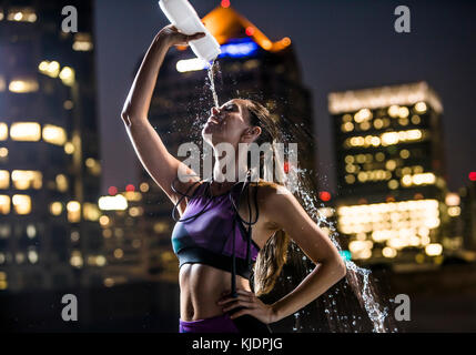 Kaukasische Frau sprühen Wasser auf Gesicht in der Stadt bei Nacht Stockfoto