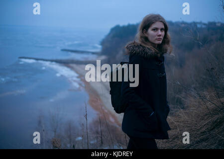 Kaukasische Frau mit Mantel auf einer Klippe in der Nähe von Ocean Stockfoto