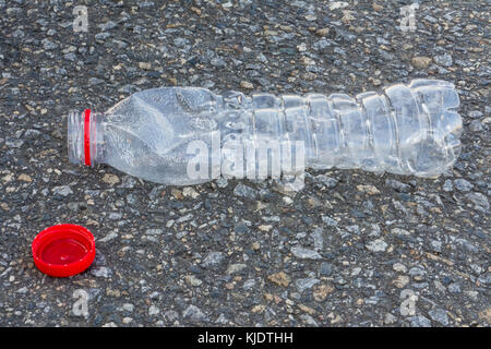 Plastikflasche mit roter Kappe. ökologische Entsorgung von Kunststoffabfällen. Transparente PET-Flasche auf Asphalt Oberfläche. Stockfoto