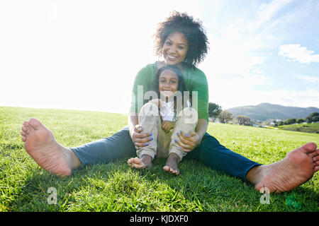 Portrait von lächelnden Mischlinge Mutter und Tochter im Gras sitzen Stockfoto