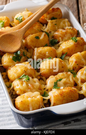 Köstliche gebackene Tater Tots mit Käse-, Fleisch- und Grünen schließen in einer Auflaufform auf den Tisch. Vertikale Stockfoto