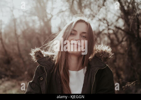 Hübsche junge europäische Frau in der grünen Jacke mit Kapuze Pelz an Kamera suchen und lächelnd. Mädchen mit langen blonden Haaren, Augenbrauen, vollen Lippen. Stockfoto