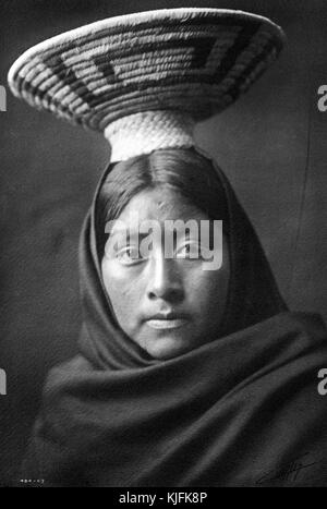 Ein fotografisches Porträt einer indianischen Frau, die in Stoff drapiert gezeigt wird und einen gewebten Korb auf dem Kopf hat, war sie Teil der Tohono O'odham Volk, sie sind eine indigene Gruppe, die vor allem in Ost-Arizona und im Nordwesten Mexikos, 1907. Aus der New York Public Library. Stockfoto