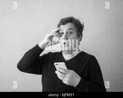 Schwarz-weiß Foto von überrascht im mittleren Alter kaukasischer Mann mit Smartphone Stockfoto