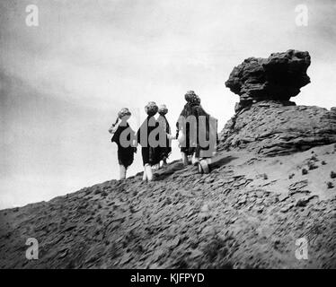 Foto von fünf indianischen Frauen, die in der Wüste spazieren, Keramiktöpfe gefüllt mit Wasser auf ihren Köpfen, mit dem Titel „Acoma Water Carriers, Acoma Girls back to the mesa Top with filled Jars“, von Edward S. Curtis, 1904. Aus der New York Public Library. Stockfoto