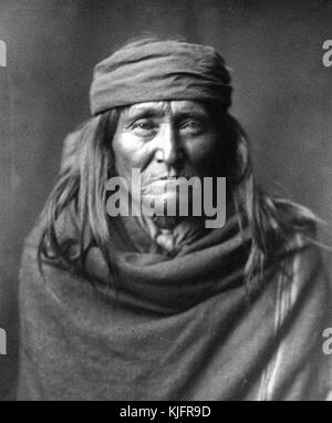 Porträt eines reifen Indianers mit langen Haaren, einem Kopfband und eingewickelt in eine Decke mit dem Titel "Eskay De, A typical, hrewd, old Apache", von Edward S Curtis, 1903. Aus der New York Public Library. Stockfoto