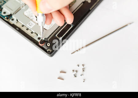 Blick von oben auf die eine Hand mit einem Schraubendreher über zerlegt Notebook und Schrauben gegen den weißen Hintergrund. Elektronik Professional Service Konzept. Stockfoto