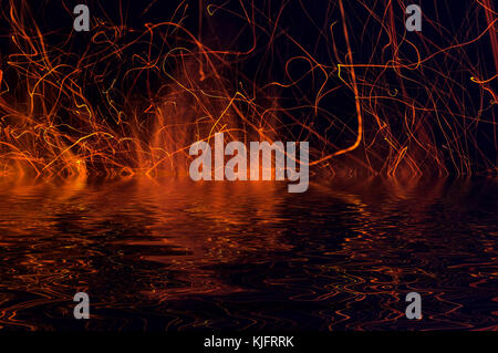 Flammen von Feuer und Funken auf einem schwarzen Hintergrund mit Reflexion im Wasser Stockfoto