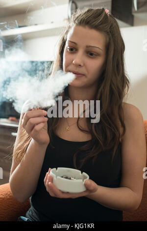 Mädchen raucht und hält Aschenbecher. Rauchen Zigarette im Haus. Stockfoto