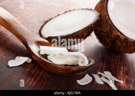 Kokosöl und Flocken im Löffel auf Holztisch. Reif halb Kokosnuss auf Holz- Hintergrund. Stockfoto