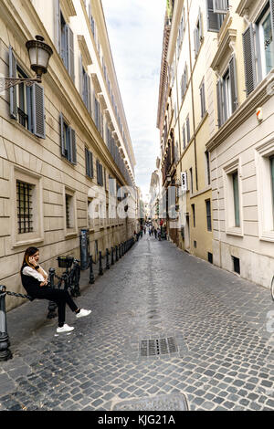 Rom, Latium, Italien. 22. Mai 2017: Junge Frau, die am Telefon spricht, sitzt auf einer Kette in der Straße namens "Via Borgognona", in der Nähe des Plaza von Spanien Stockfoto