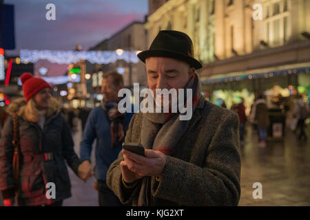 Reifer Mann genießt einen Abend an Weihnachten durch die Stadt schlendern. Er hat gestoppt sein Smartphone zu verwenden. Stockfoto