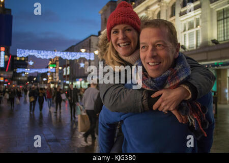 Reifer Mann schenkt seiner Frau einen Huckepack durch die Innenstadt zur Weihnachtszeit. Stockfoto