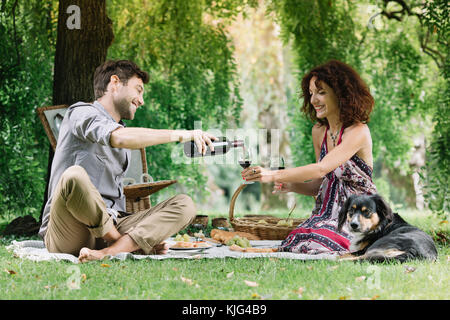 Paar mit Hund bei einem Picknick im Park trinken Rotwein Stockfoto