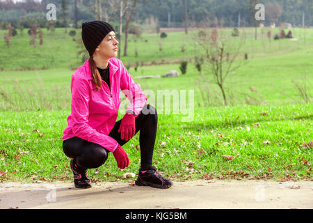 Junge Frau Analyse der Anschluss vor der Ausführung an einem kalten Wintertag auf der Spur eines städtischen Park. weiblichen Athleten mit Rosa windbreaker, b Stockfoto