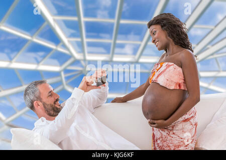 Schöner Mann nimmt Fotos mit Smartphone von Jungen glücklich Schwangere Frau Wohnzimmer Stockfoto