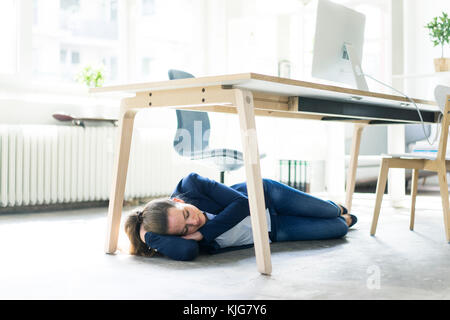 Geschäftsfrau unter dem Tisch im Büro schlafen liegen Stockfoto