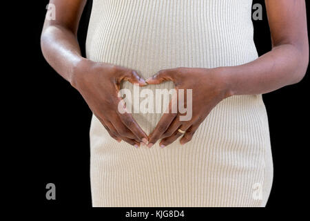Bauch von Schwangeren, Frau ihre Hände halten in Form eines Herzens auf ihrem Baby bump mit Fingern, Nahaufnahme Stockfoto
