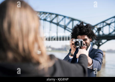 Lächelnd Mann im Anzug am Flußufer ein Bild von seiner Freundin mit einem Vintage Kamera Stockfoto