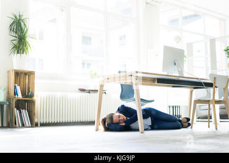 Geschäftsfrau unter dem Tisch im Büro schlafen liegen Stockfoto