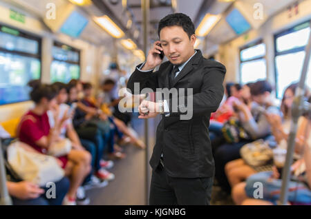 Asiatische Geschäftsmann Aufruf Mobiltelefon über die abstrakte verschwommenes Foto von Passagieren, die mit dem Smart Phone oder Tabletten sind in Sky Train, Business te Stockfoto