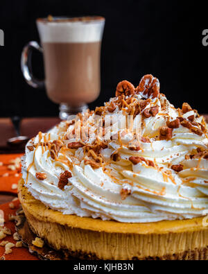 Genießen Thanksgiving mit einem Kürbis kuchen Käsekuchen und eine Tasse Milchkaffee Kaffee. Einstellung auf eine orange Leaf placemate mit Löffel und pie Messer. Käsekuchen Stockfoto