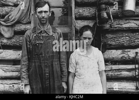 Schwarz-weiß-Foto eines Mannes und einer Frau, die nebeneinander stehen, vor einem Blockhaus, von Ben Shahn, gebürtiger Litauer, amerikanischer Künstler, der für seine Arbeit für die Farm Security Administration bekannt ist, die die Auswirkungen der Großen Depression im Boone County, Arkansas, Oktober 1935 dokumentiert. Aus der New York Public Library. Stockfoto