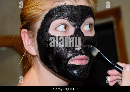 Mädchen in einem kosmetischen schwarze Maske. reinigende Maske von Aspirin und Aktivkohle. Schwarz kosmetische Gesichtsmaske Stockfoto