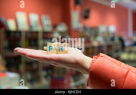 Frau halten puzzle Wort PR in der Buchhandlung. Stockfoto