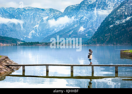 Reiseziel Thema Bild mit einer Frau, die zu Fuß auf einem schmalen Deck, überquert den Hallstätter See, inmitten der österreichischen Alpen Berge umgeben. Stockfoto