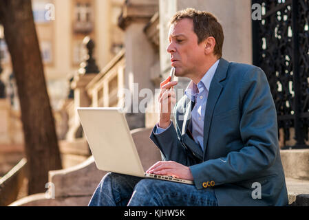 Ein mittleres Alter Geschäftsmann Standortwahl auf der Treppe mit einem Laptop und ein Handy in der Hand und Denken Stockfoto