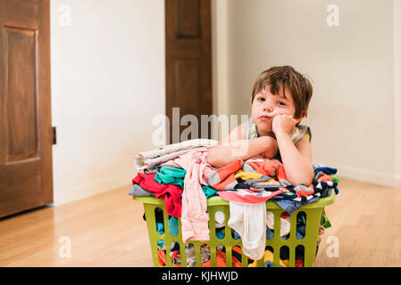 Junge sitzt auf dem Boden lehnte sich auf der Wäsche Korb gefüllt mit Kleidung Stockfoto