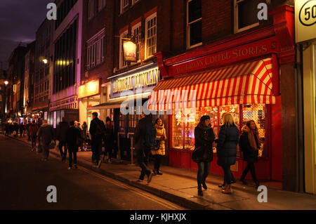 Menschen zu Fuß vorbei an Geschäften und Bars in der Nacht auf Old Compton Street in Soho, London, England Stockfoto