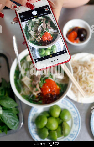 Schüssel vietnamesische Nudelsuppe Pho genannt. Frau, die Bild mit Smartphone Ihrer Mahlzeit. Ho Chi Minh City. Vietnam. Stockfoto