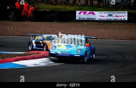 Ein paar Porsche Rennwagen Wettbewerb eine Ecke in der britischen Tourenwagen Meisterschaften an der Rennstrecke Knockhill Racing Circuit. Stockfoto