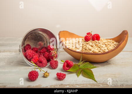 Frische Himbeeren in einen Eimer und Haferflocken in eine hölzerne Schüssel auf einem rustikalen Holzmöbeln Hintergrund. gesunde Ernährung, Vegetarische Konzept Stockfoto