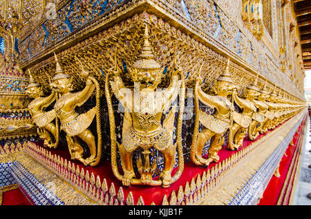 Entlang der Innenwände des Bangkok-Palastkomplexes Wat Phra Kaew-Tempel halten ein Fries vergoldeter Garudas die Naga-Schlangen zum Schutz des Tempels fest. Stockfoto