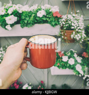 Nahaufnahme der Frau hand mit Vintage Kaffeebecher gegen Topfpflanzen und Blumen Stockfoto