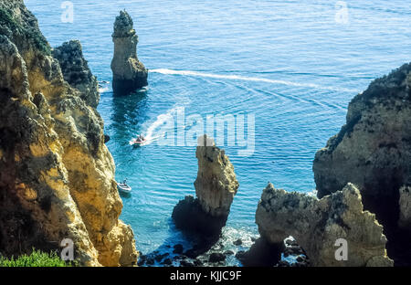 Clifftop Blick auf die Boote segeln durch die markanten Felsformationen an der Küste der Algarve, Portugal. Stockfoto