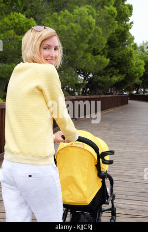 Lächelnde Mutter Bummeln ein Baby im Wagen Stockfoto