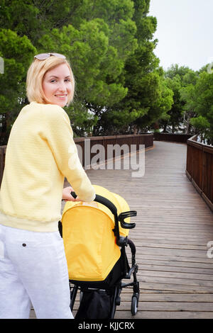 Lächelnde Mutter Bummeln ein Baby im Wagen Stockfoto